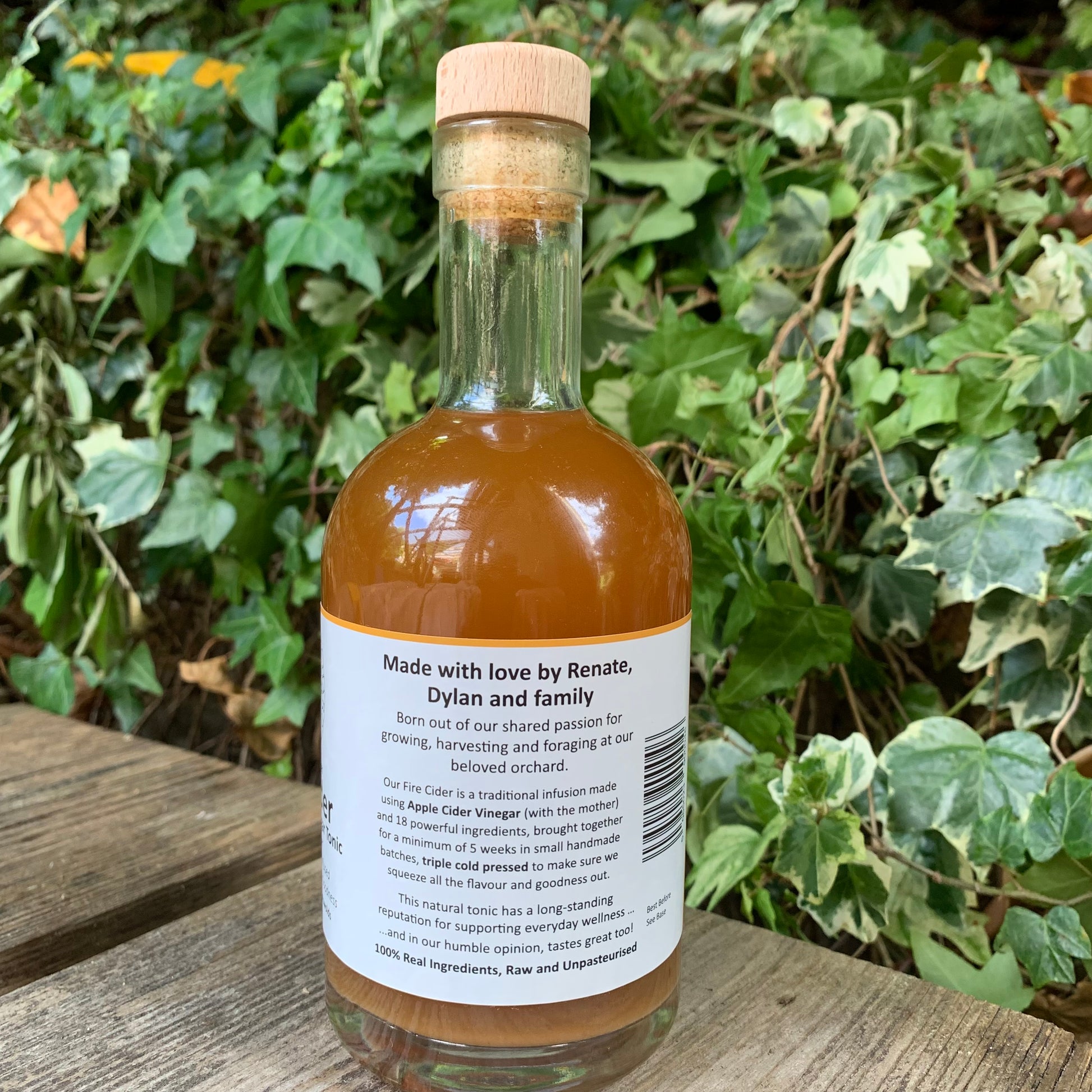 Back label of Bee Sweet Fire Cider 350ml – handcrafted apple cider vinegar tonic made by Renate, Dylan and family, set on a rustic wooden surface with leafy garden background