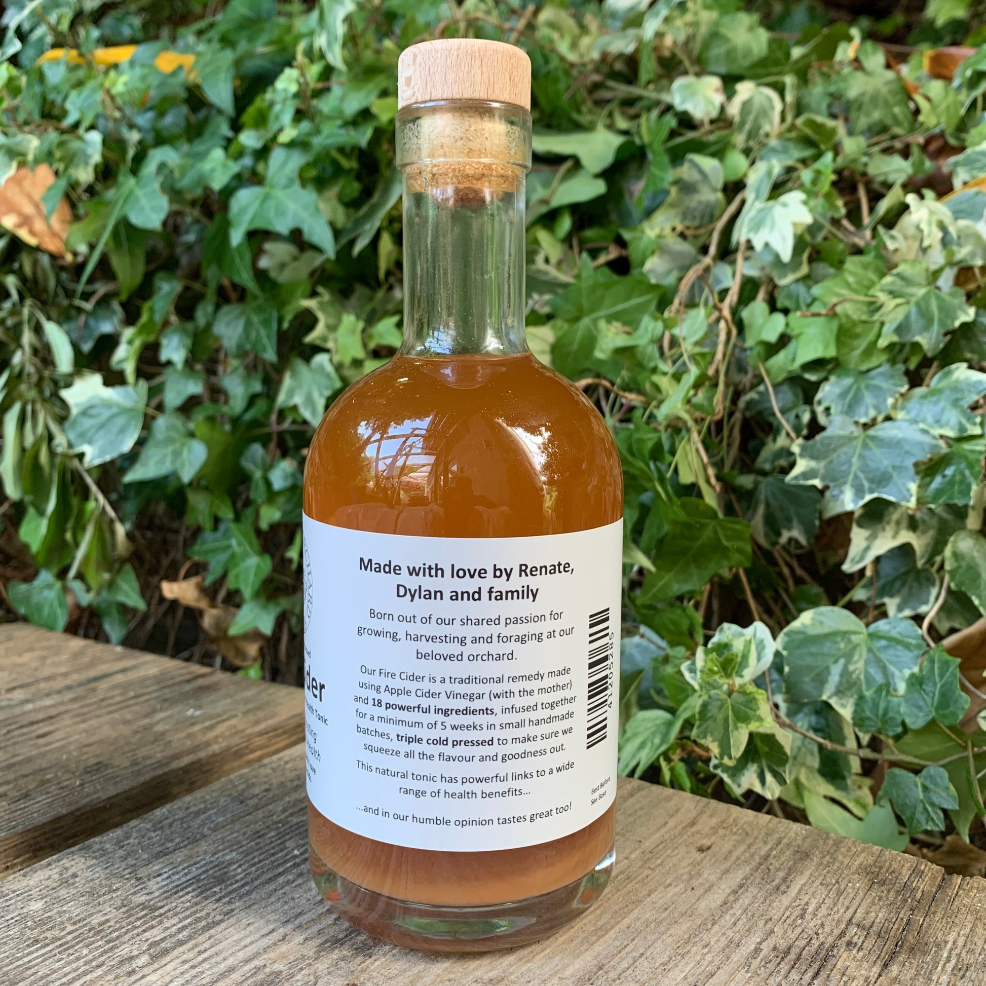 Back label of Original Fire Cider 350ml – artisan apple cider vinegar tonic made by Renate, Dylan and family, photographed outdoors with ivy-covered backdrop