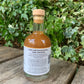 Angled view of Bee Sweet Fire Cider bottle – artisan health tonic made with raw honey and spices, photographed in natural garden setting with ivy backdrop