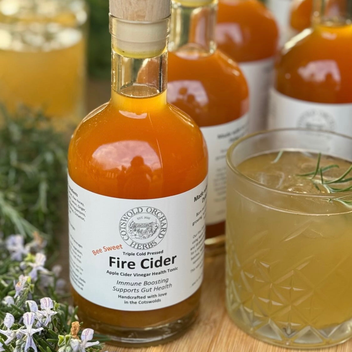 Bottle of Fire Cider with a glass of liquid and herbs on a wooden surface