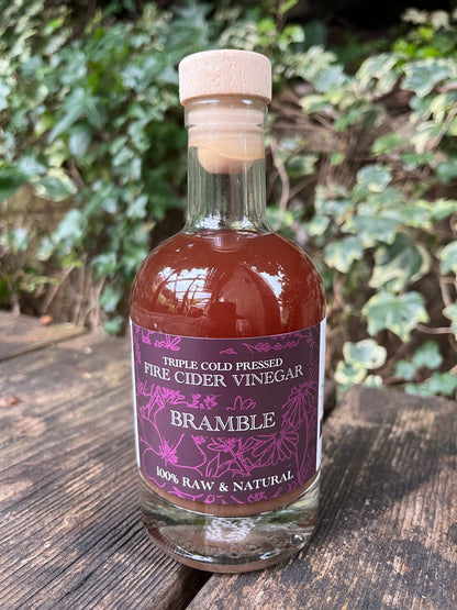 Bottle of Bramble Fire Cider Vinegar on a wooden surface with greenery in the background