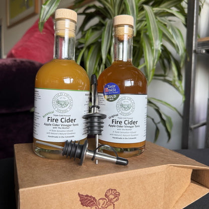 Two bottles of Fire Cider on a wooden surface with a plant in the background
