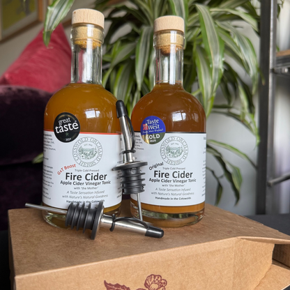 Two bottles of Fire Cider on a cardboard box with a plant in the background