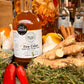Bottle of 'Great Taste' Fire Cider surrounded by ingredients like ginger and peppers on a wooden surface.