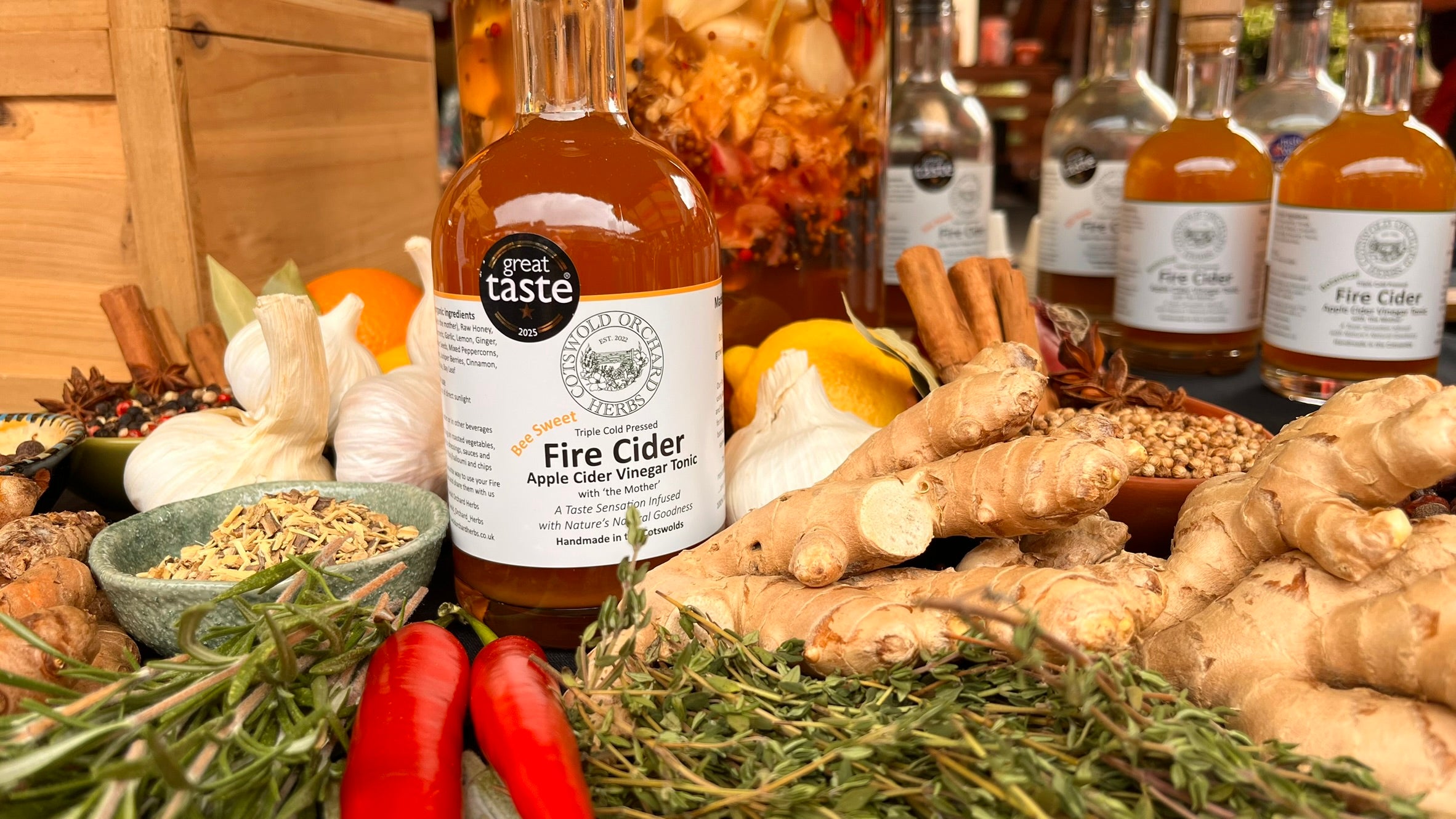 Bottle of 'Great Taste' Fire Cider surrounded by ingredients like ginger and peppers on a wooden surface.
