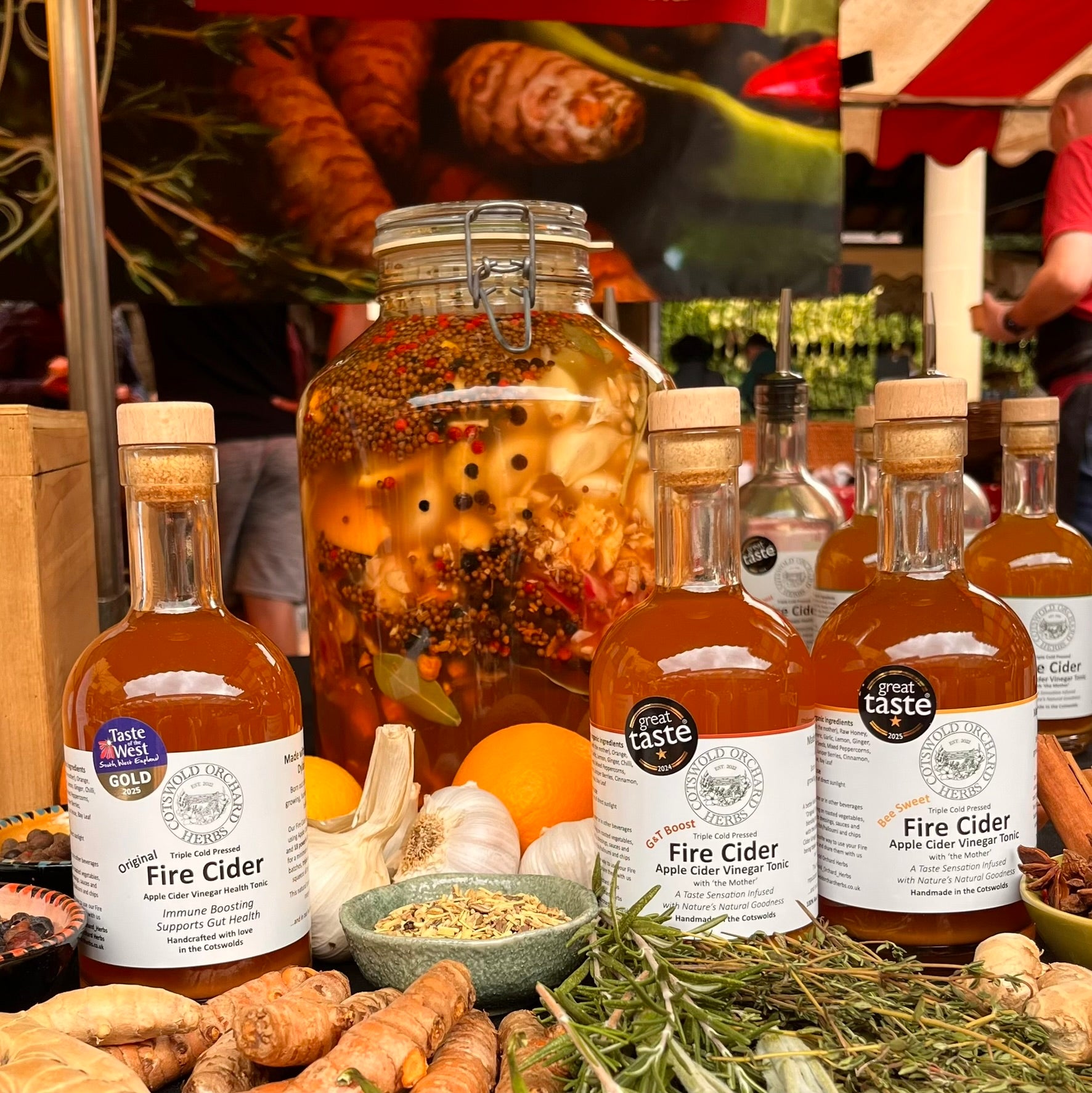 Bottles of 'Great Taste' Fire Cider with ingredients on a market stall background