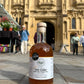 Bottle of Fire Cider vinegar with a label in front of an historic church in the centre of Cirencester.
