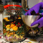 Glass jar filled with a colorful salad and a hand holding a metal bowl on a patterned tablecloth.