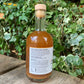 Side view of Bee Sweet Fire Cider 350ml bottle – label showing organic ingredients and usage directions, placed outdoors on a wooden bench surrounded by ivy