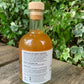 Side label of G&T Boost Fire Cider 250ml – showing list of organic ingredients, how to use instructions, and brand website, bottle placed outdoors with ivy-covered backdrop