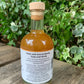 Back label of G&T Boost Fire Cider 250ml – handcrafted tonic made with apple cider vinegar, turmeric, garlic, and ginger, created by Renate, Dylan and family, set on a wooden bench with leafy background