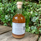 Back label of Original Fire Cider 500ml – natural health tonic made with love by Renate, Dylan and family, photographed outdoors in a green leafy garden setting