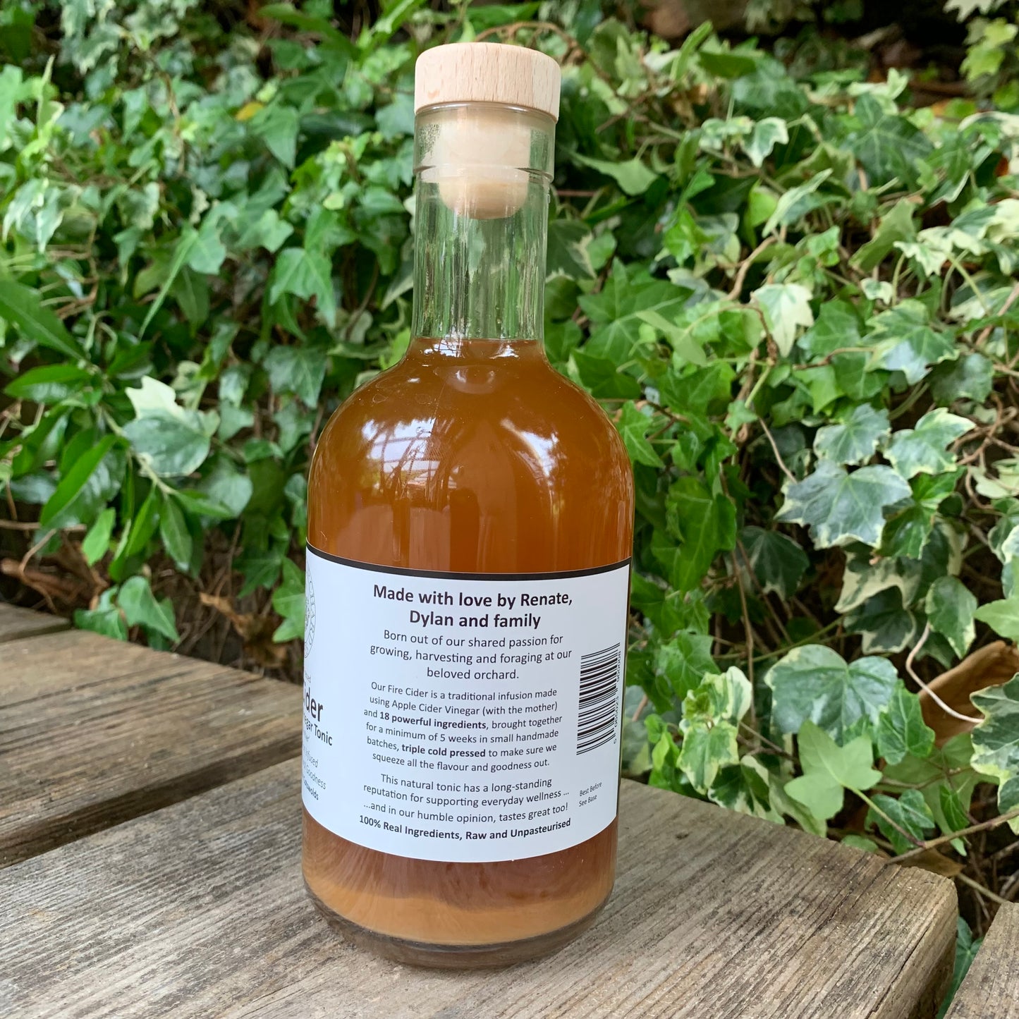 Back label of Original Fire Cider 500ml – natural health tonic made with love by Renate, Dylan and family, photographed outdoors in a green leafy garden setting